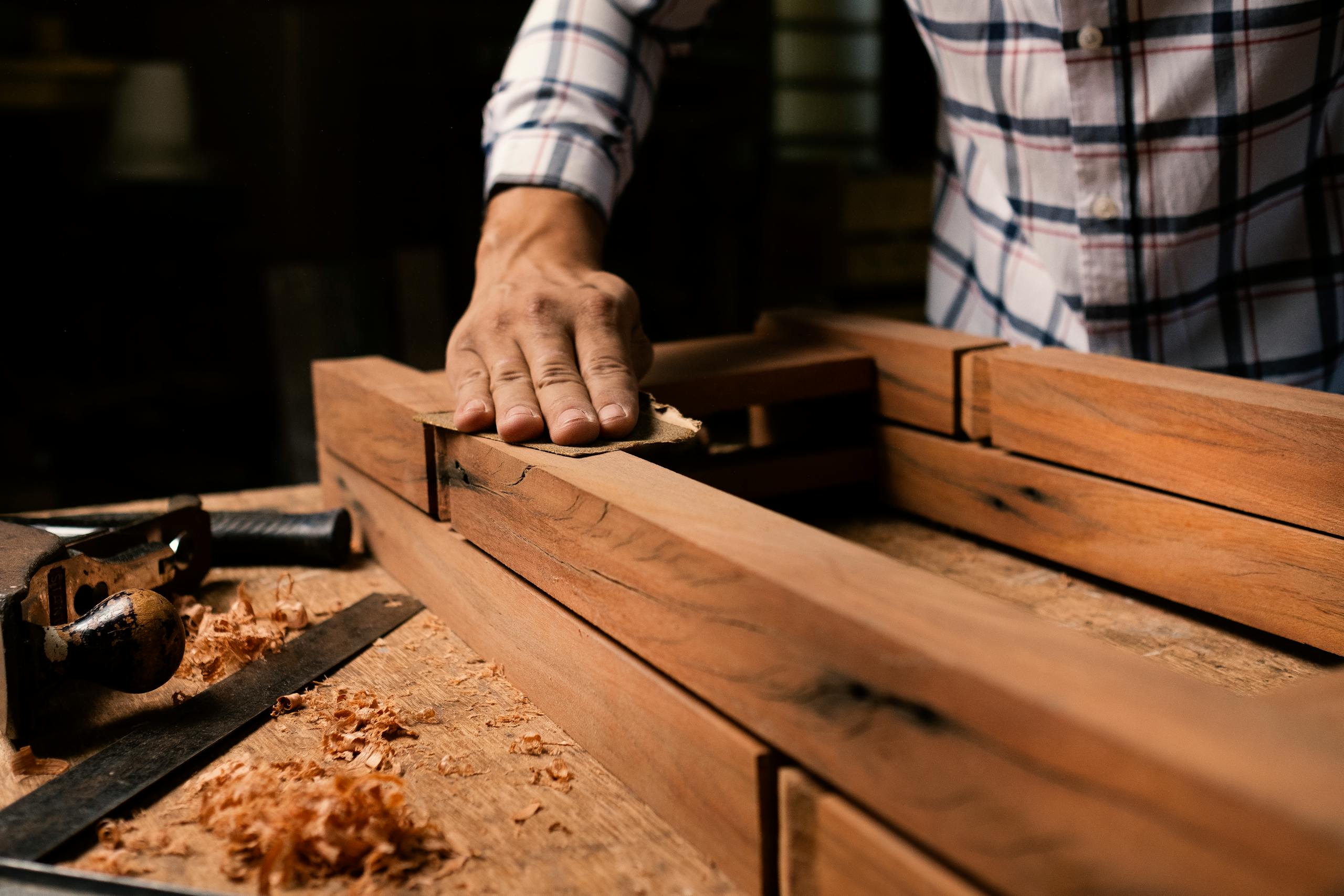 A close-up of a woodworker smoothing a wooden frame by hand in a woodworking shop.
