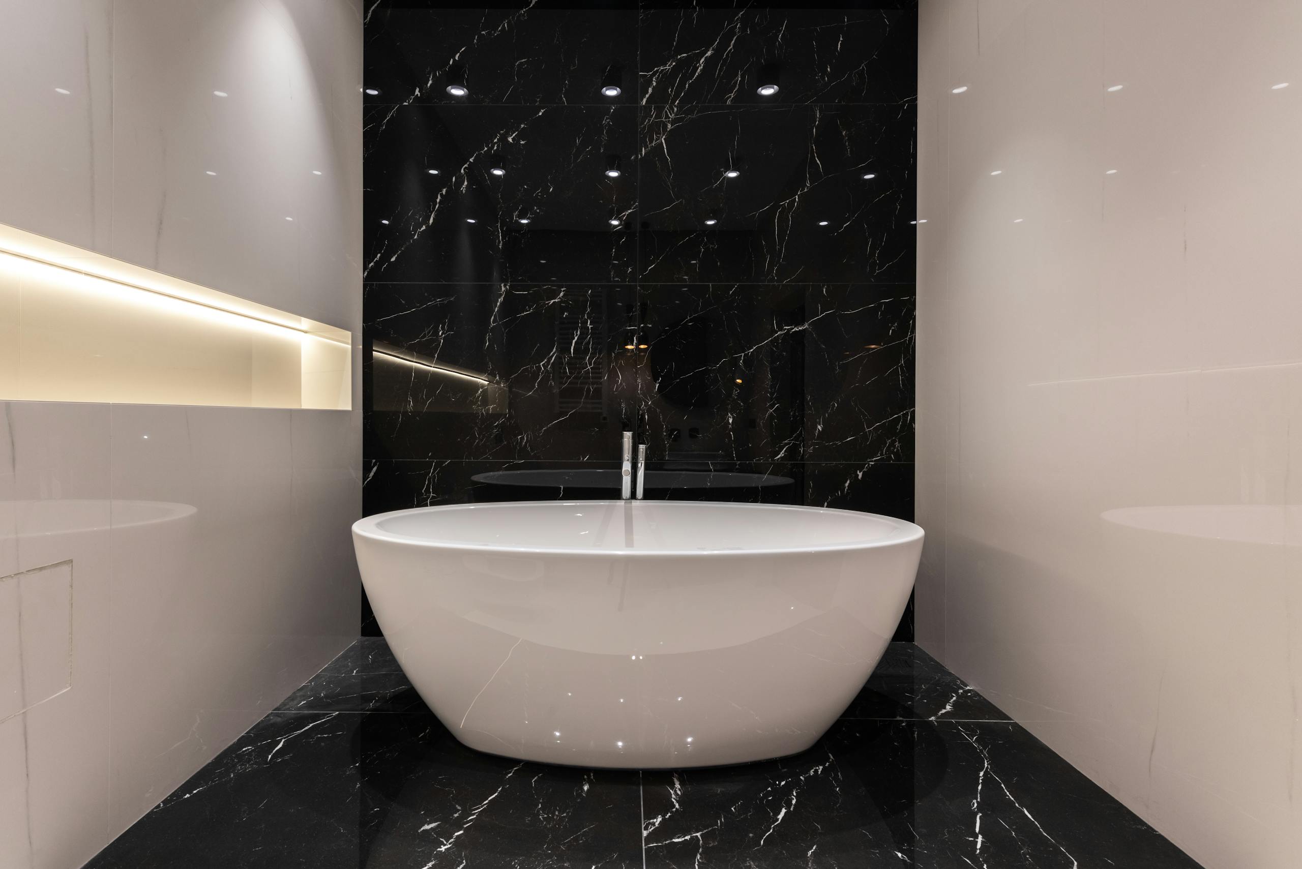 Interior of empty comfortable modern bathroom with black and white marble tile and soaker bath