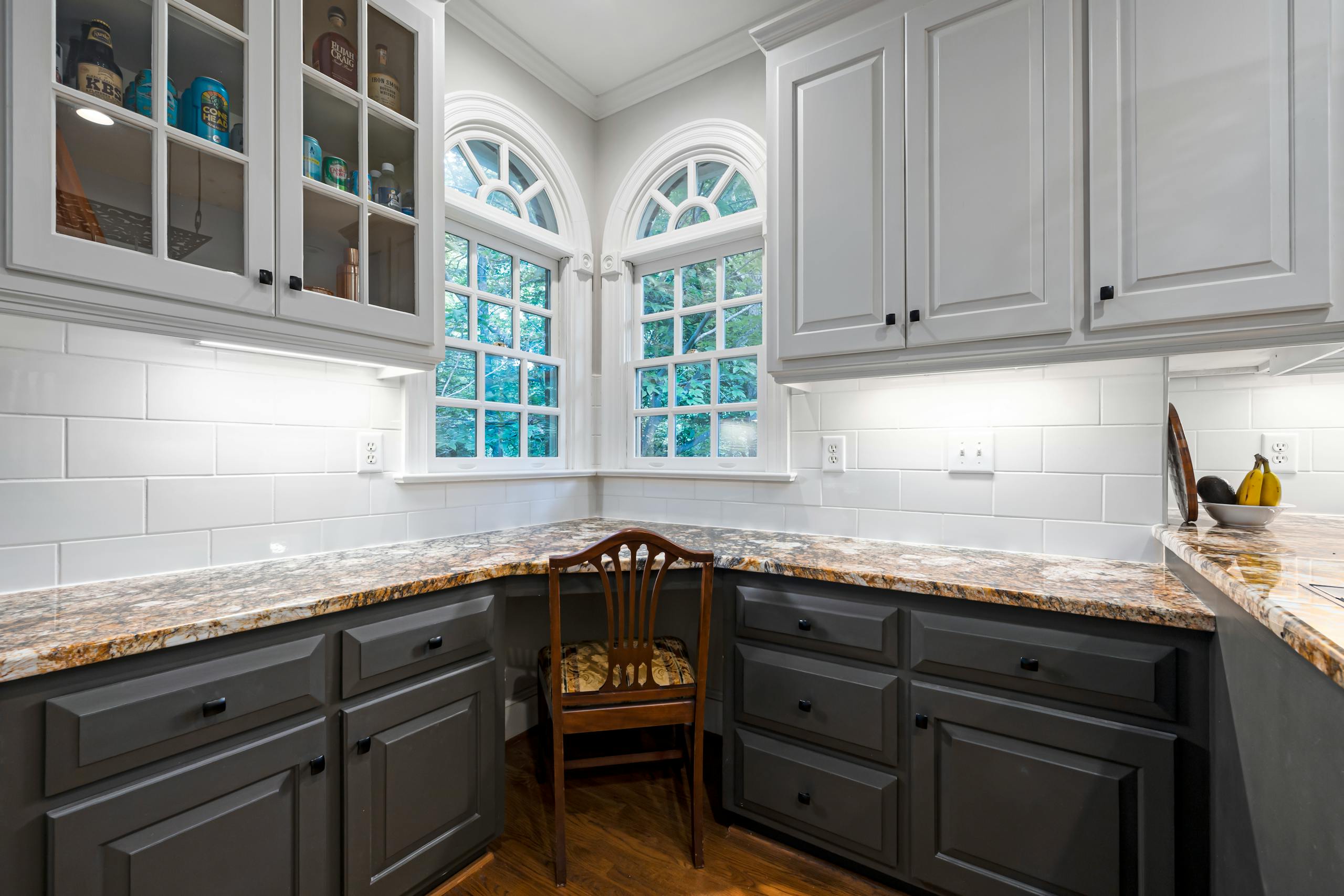 Modern kitchen interior featuring granite countertops, white cabinets, and arched windows.